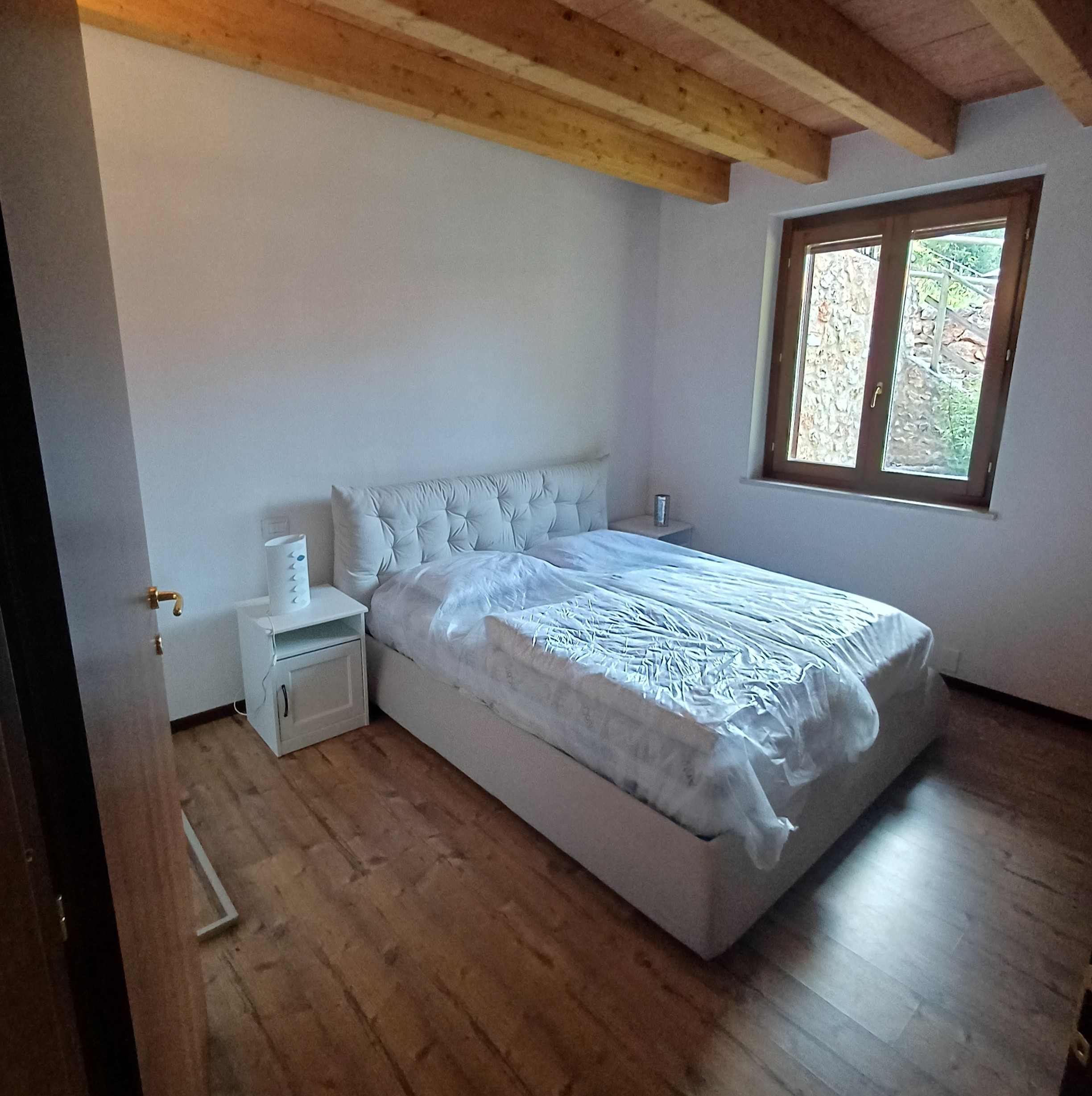 Camera matrimoniale luminosa con letto imbottito e travi in legno